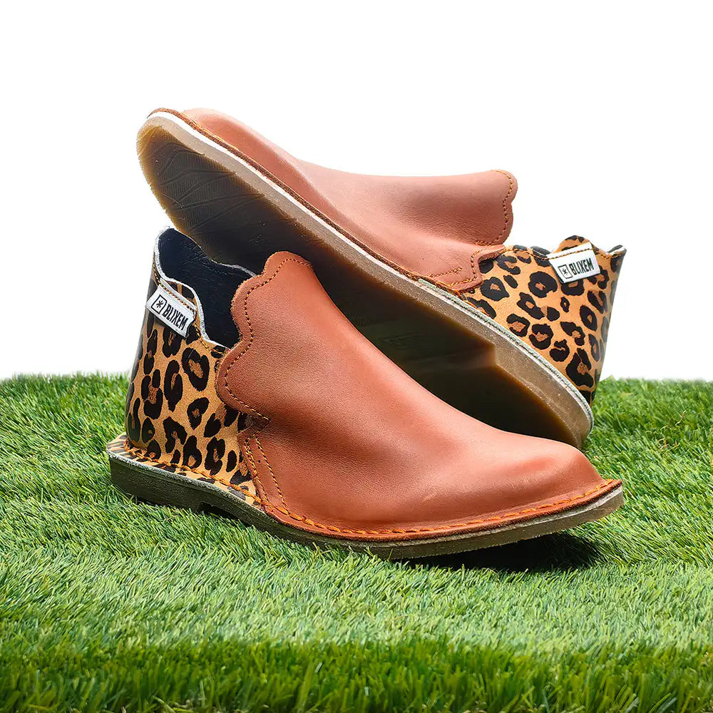Brown leather shoes with leopard print soles on a grass background
