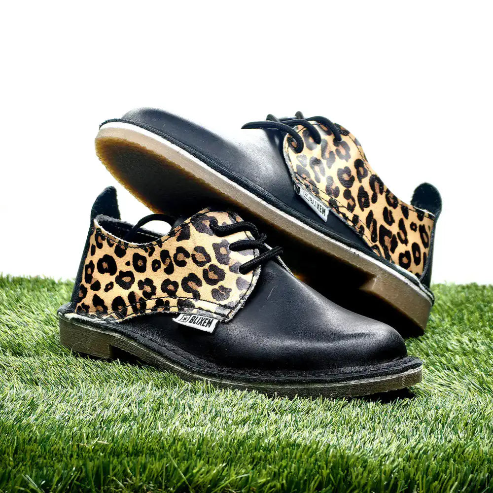 Black shoes with leopard print tan soles on a grass background