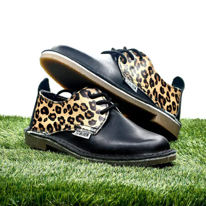 Black shoes with leopard print tan soles on a grass background