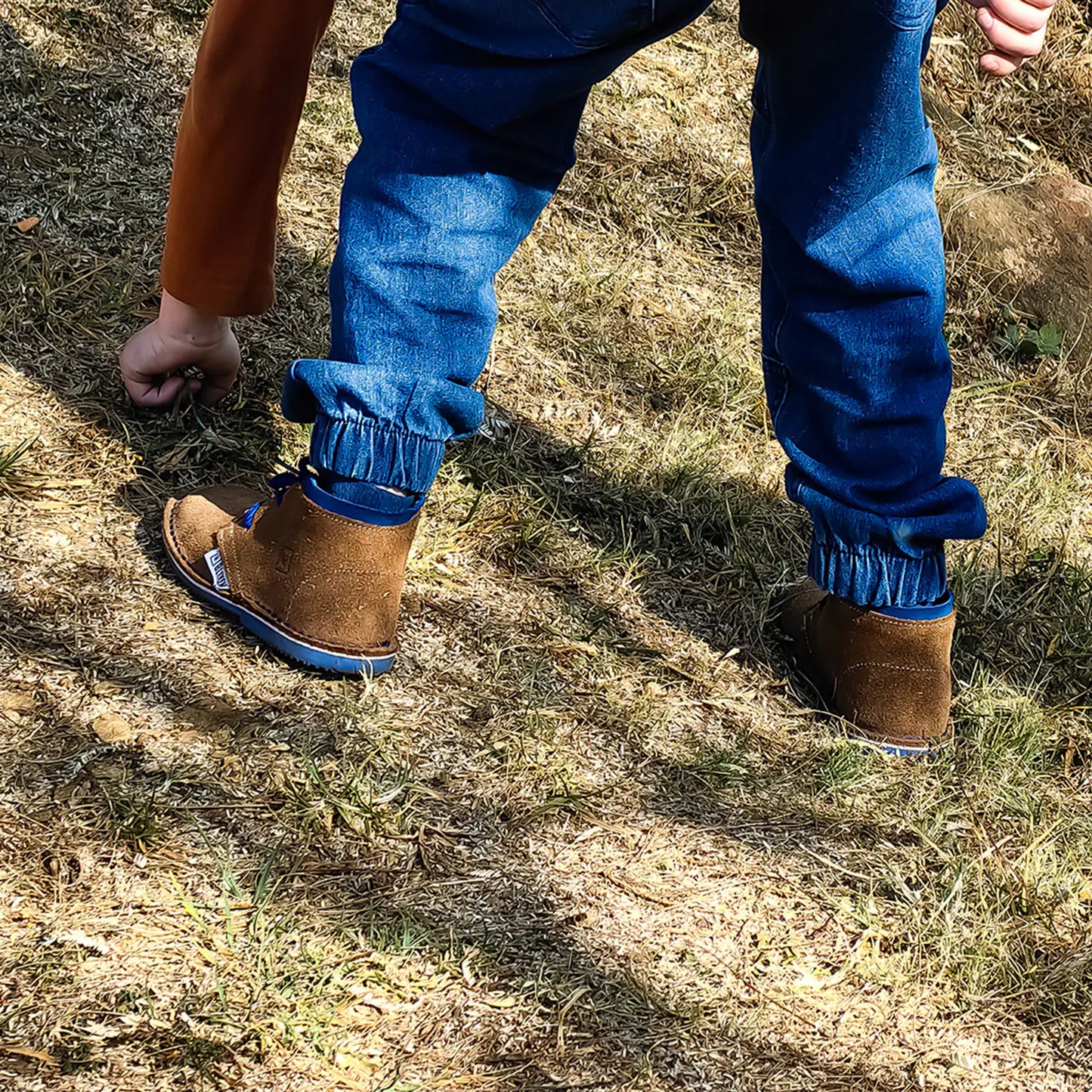 Person wearing blue pants with cuffed ankles and brown boots on a grassy ground.