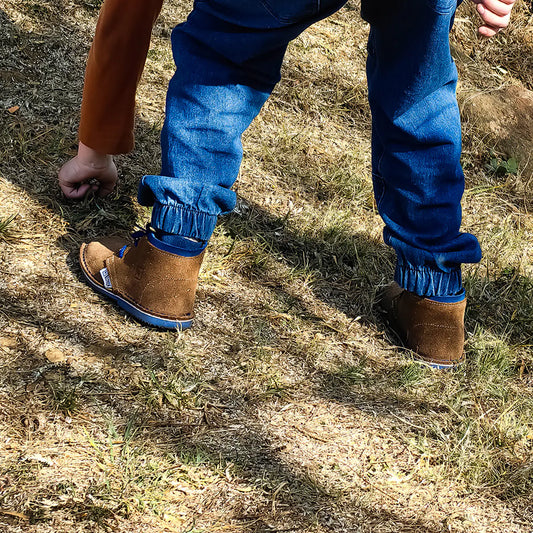 Person wearing blue pants with cuffed ankles and brown boots on a grassy ground.