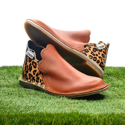 Brown leather shoes with leopard print soles on a grass background