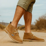 Person wearing brown suede shoes with a desert landscape background
