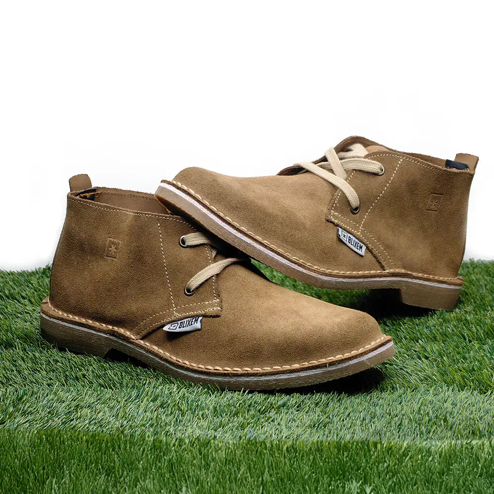 Pair of brown suede boots on grass with a white background