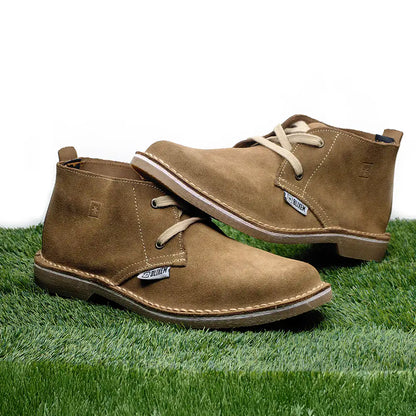 Pair of brown suede boots on grass with a white background