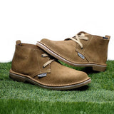 Pair of brown suede boots on grass with a white background