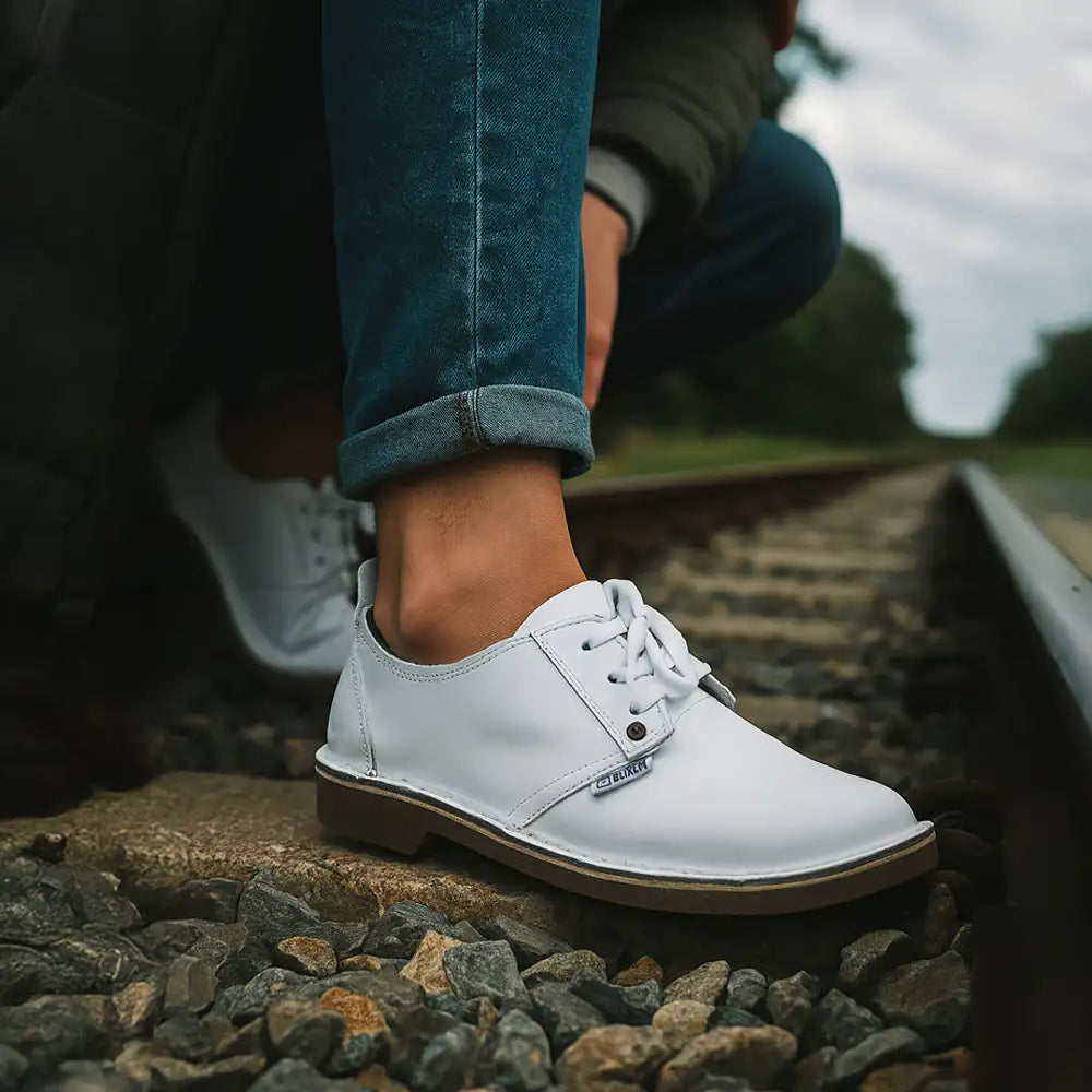 White leather shoe with brown sole on a rocky surface